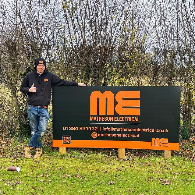 Electrician smiling and giving the thumbs up next to a Matheson Electrical sign