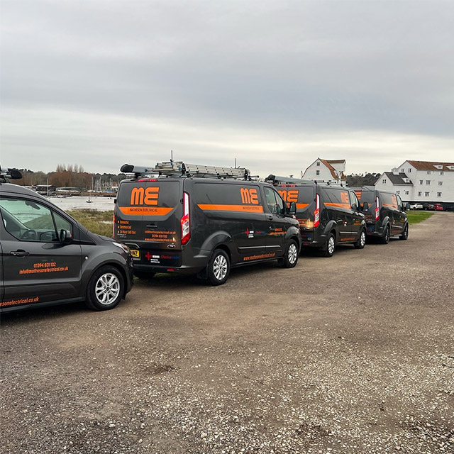 Four vans with Matheson Electrical Ltd branding parked on road with Woodbridge Tide Mill in the background